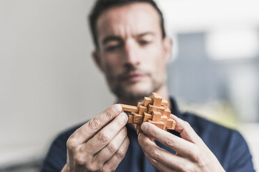 Mature man sitting in office assembling wooden cube puzzle - UUF15811
