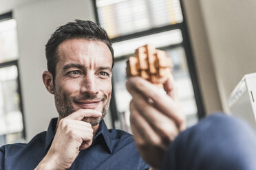 Mature man sitting in office assembling wooden cube puzzle - UUF15813