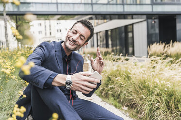 Businessman sitting outside, taking a break, listening music from his smartphone - UUF15818