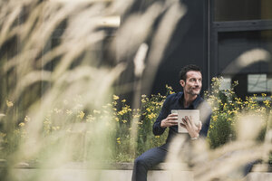 Businessman sitting outside, taking a break, drinking coffee, using digital tablet - UUF15822