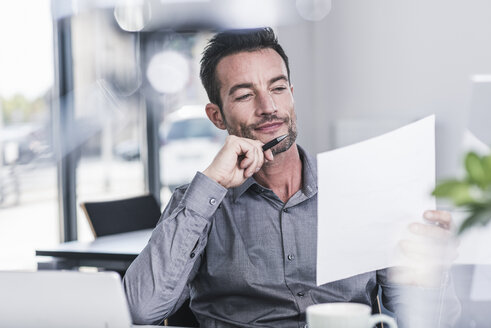 Businessman sitting in office, reading a letter - UUF15838