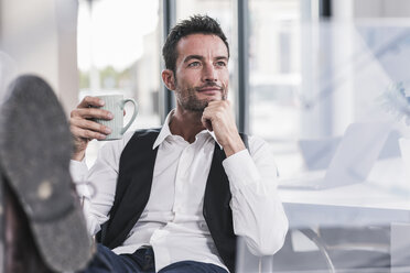 Businessman sitting in office, drinking coffee, with feet up - UUF15852