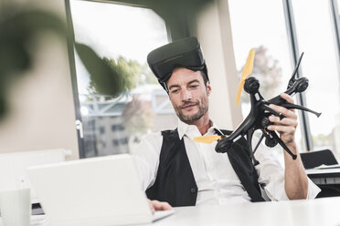 Geschäftsmann sitzt im Büro und arbeitet an einer Drohne, mit VR-Brille - UUF15853