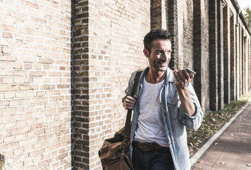 Mature man commuting in the city, carrying abg and smartphone - UUF15865