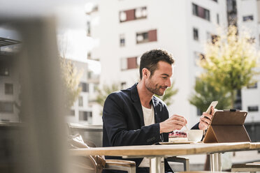 Businessman sitting in cafe, drinking coffee, using smartphone - UUF15875