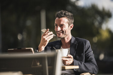 Geschäftsmann sitzt in einem Café, trinkt Kaffee und benutzt sein Smartphone - UUF15878