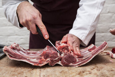 A butcher using a sharp knife to prepare lamb ribs for rack of lamb. - MINF09093