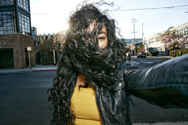 Porträt einer jungen Frau mit langen lockigen schwarzen Haaren, die auf der Straße steht und in die Kamera schaut. - MINF09102