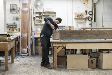 Kaukasischer männlicher Tischler bei der Arbeit an einem großen Schrank in einer Holzverarbeitungsfabrik - MINF09118