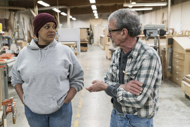 Ein älterer weißer Schreiner und eine schwarze Schreinerin besprechen ein Projekt in einer großen Holzverarbeitungsfabrik. - MINF09128