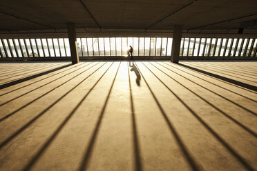 Ein Geschäftsmann erkundet bei Sonnenuntergang einen neuen leeren Geschäftsraum für ein neues Büro, während das Sonnenlicht durch die Glaswand fällt. - MINF09158