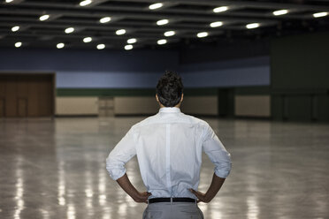 A businessman standing in a dimly lit and dark exhibition area in a convention centre. - MINF09191