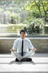 Ein Geschäftsmann macht eine meditative Pause in einem Raum voller Zimmerpflanzen. - MINF09196