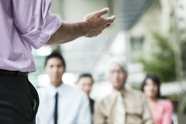 A closeup of a hand gesturing to a group of business people in a meeting. - MINF09199