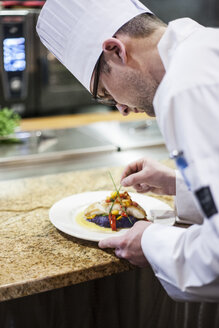 A Caucasian male chef putting the finishing touches on a plate of fish in a commercial kitchen. - MINF09209