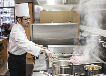 Ein asiatischer Koch bei der Arbeit mit frischem Fleisch auf dem Grill in einer Großküche, - MINF09213