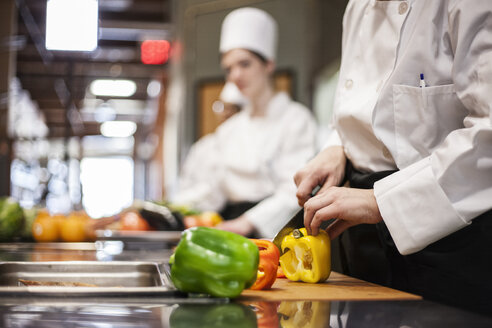 A closeup of the hands of a chef cutting vegetables in a commercial kitchen. - MINF09214