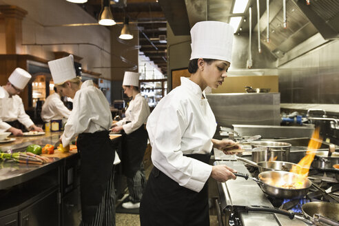 A crew of chef's working in a commercial kitchen, with a black chef in the foreground sauteing vegetables. - MINF09217