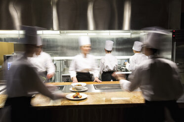 Ein unscharfer Blick auf ein Team von Köchen, die in einer Großküche arbeiten. - MINF09219