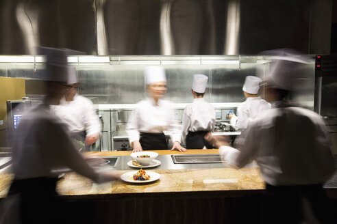 A blurred view of a crew of chefs working around a commercial kitchen. - MINF09219