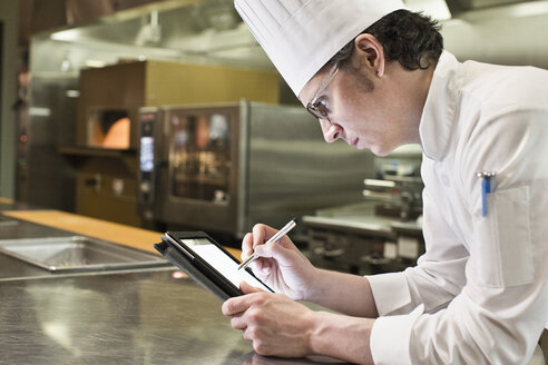 A Caucasian male chef working on a notebook computer in a commercial kitchen. - MINF09221