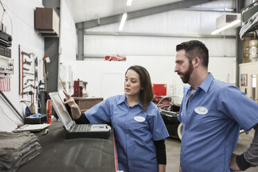 Two mechanics working on a laptop computer in a repair shop. - MINF09226