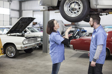 Two Caucasian male and female car mechanics at work on a car in a classic car repair shop. - MINF09229