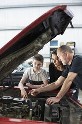 Ein älterer kaukasischer Automechaniker spricht mit einer kaukasischen Mutter und ihrem Sohn über eine Motorreparatur in einer Oldtimerwerkstatt. - MINF09232