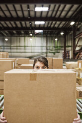 A Caucasian female warehouse worker behind a cardboard box in a distribution warehouse. - MINF09244