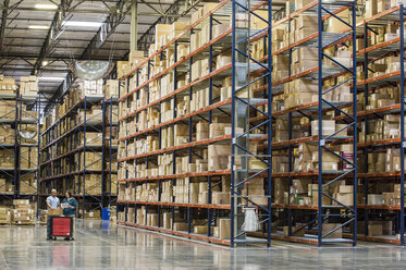 Two employees checking inventory beside racks of boxes in temporary storage in a distribution warehouse. - MINF09256