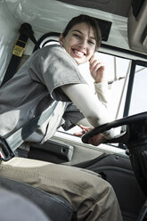 Portrait of a uniformed Caucasian female truck driver at the wheel of her truck at a distribution warehouse. - MINF09257