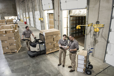 Ein Team von drei uniformierten Lagerarbeitern in gemischten Rassen, die in einem Auslieferungslager verpackte Produkte in einen Lastwagen laden. - MINF09258