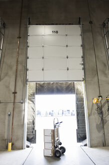 A hand truck stacked with boxes sitting in the open doorway to a loading dock in a distribution warehouse. - MINF09259