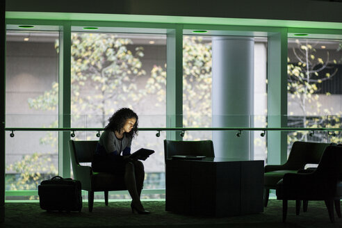 Eine schwarze Geschäftsfrau sitzt vor den Fenstern in einer abgedunkelten Lobby eines Kongresszentrums. - MINF09262