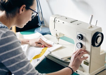 Woman using electric sewing machine to make curtains - MINF09283