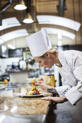 A Caucasian female chef putting the finishing touches on a plate of fish in a commercial kitchen. - MINF09292