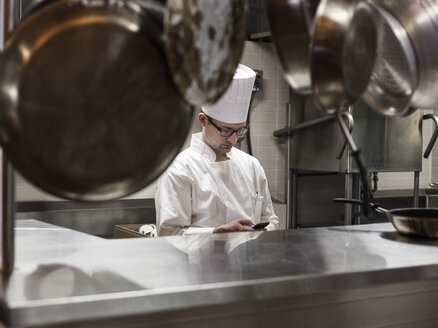 A Caucasian male chef checking his cell phone in a commercial kitchen, - MINF09296