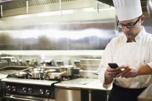 A Caucasian male chef checking his cell phone in a commercial kitchen, - MINF09297