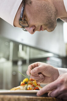 A Caucasian male chef putting the finishing touches on a plate of fish in a commercial kitchen. - MINF09299