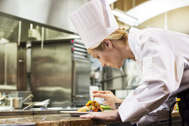 A Caucasian female chef putting the finishing touches on a plate of fish in a commercial kitchen. - MINF09300