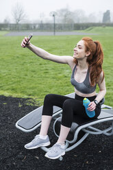 Smiling young woman with long red hair wearing sports kit, exercising outdoors. - MINF09338