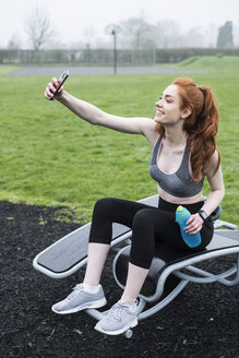 Lächelnde junge Frau mit langen roten Haaren im Sportdress, die im Freien trainiert. - MINF09338