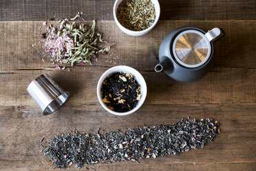 Nahaufnahme einer Auswahl von Teeblättern und einer schwarzen Teekanne auf einem Holztisch. - MINF09359