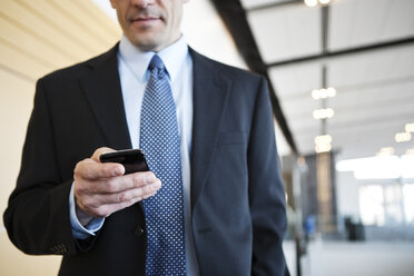 Kaukasischer Geschäftsmann, der in der Lobby eines Konferenzzentrums sein Handy überprüft. - MINF09367