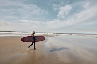 Mann im Neoprenanzug, der mit einem Surfbrett in Richtung Meer läuft - MINF09391