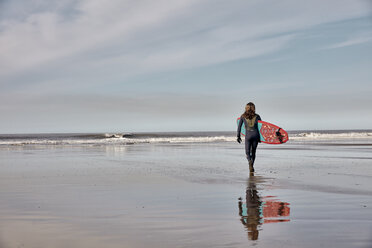 Mann mit einem Surfbrett in der Hand, der bei Ebbe auf das Meer hinausgeht. - MINF09392