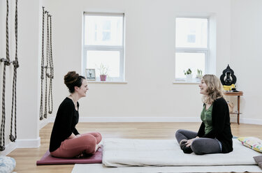 Zwei Frauen sitzen sich in einem Fitnessstudio mit gekreuzten Beinen gegenüber - MINF09393