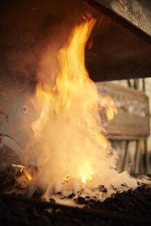 Flammen und Rauch, die von einem Schmiedefeuer in einer Metallwerkstatt aufsteigen. - MINF09404