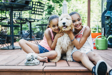 Mixed Race Sisters Play with Labradoodle Puppy on Porch - MINF09413