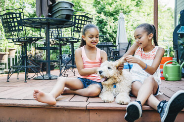 Gemischtrassige Schwestern spielen mit Labradoodle-Welpe auf Veranda - MINF09414